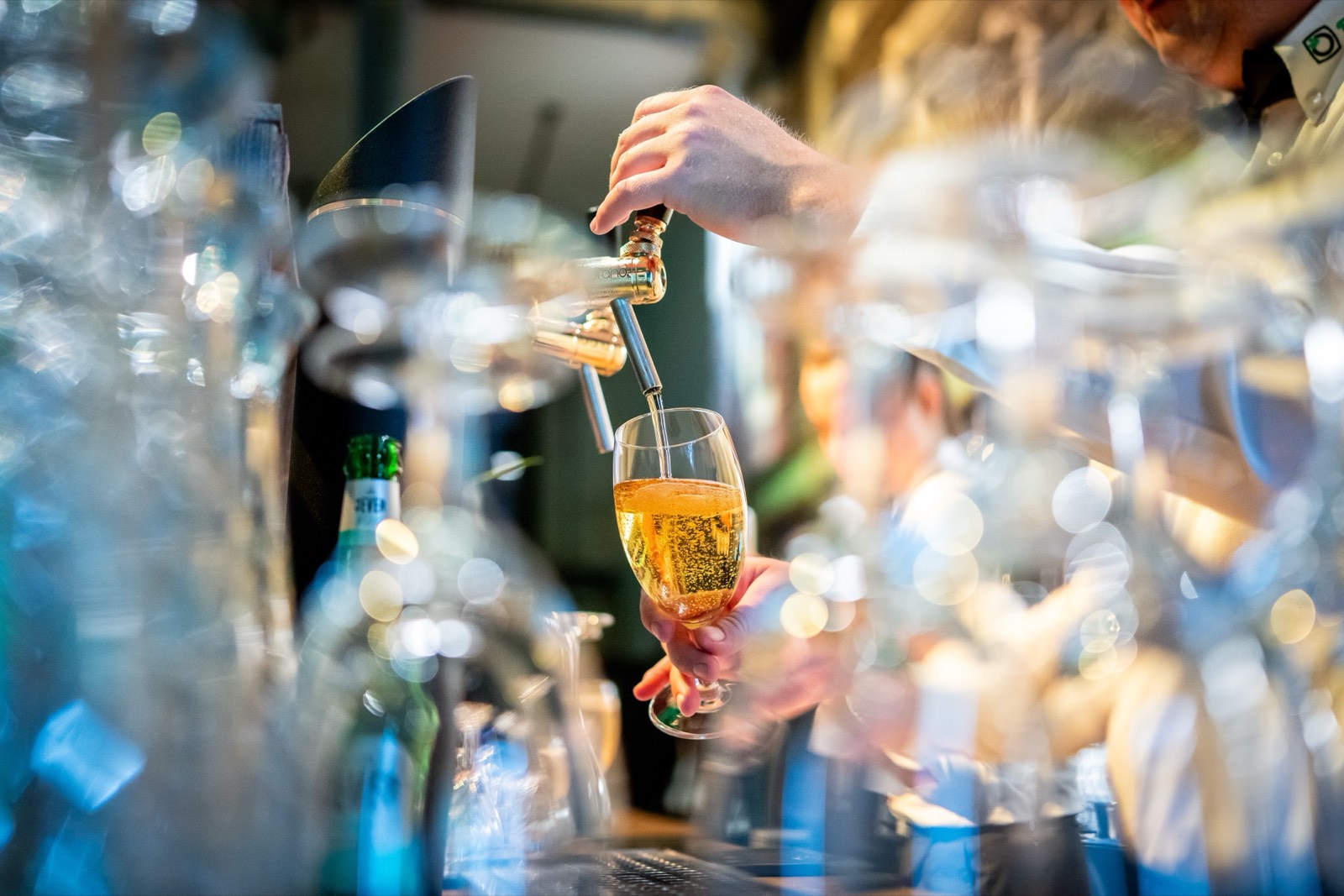 Hand am Zapfhahn füllt ein Glas, davor funkelnde Gläser an der Eventbar