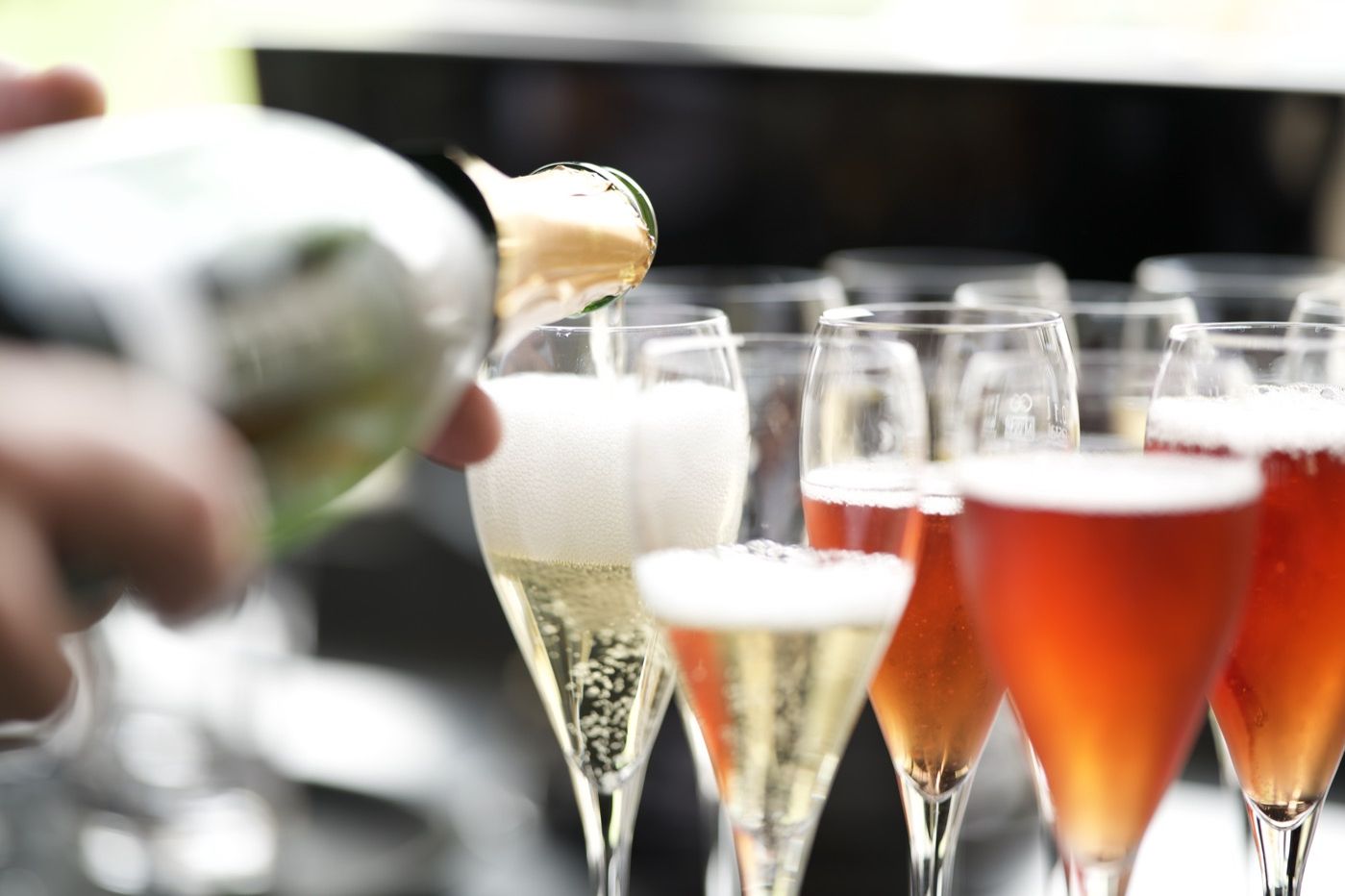 Sekt und Rosé werden aus der Flasche in eine Reihe Gläser eingeschenkt