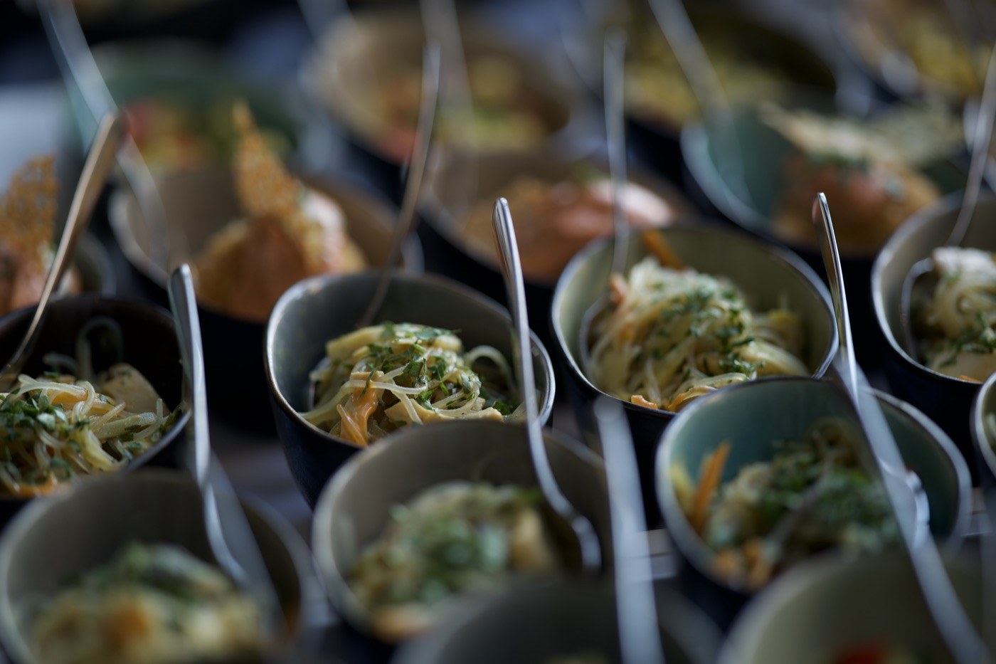 Kleine Bowls mit Nudeln, Gemüse und Kräutern in Reihen am Buffet