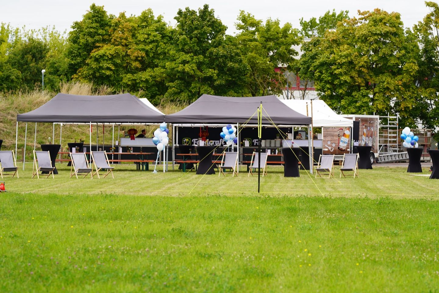 Feier auf einer Wiese mit Pavillons, Liegestühlen, Stehtischen und Luftballons