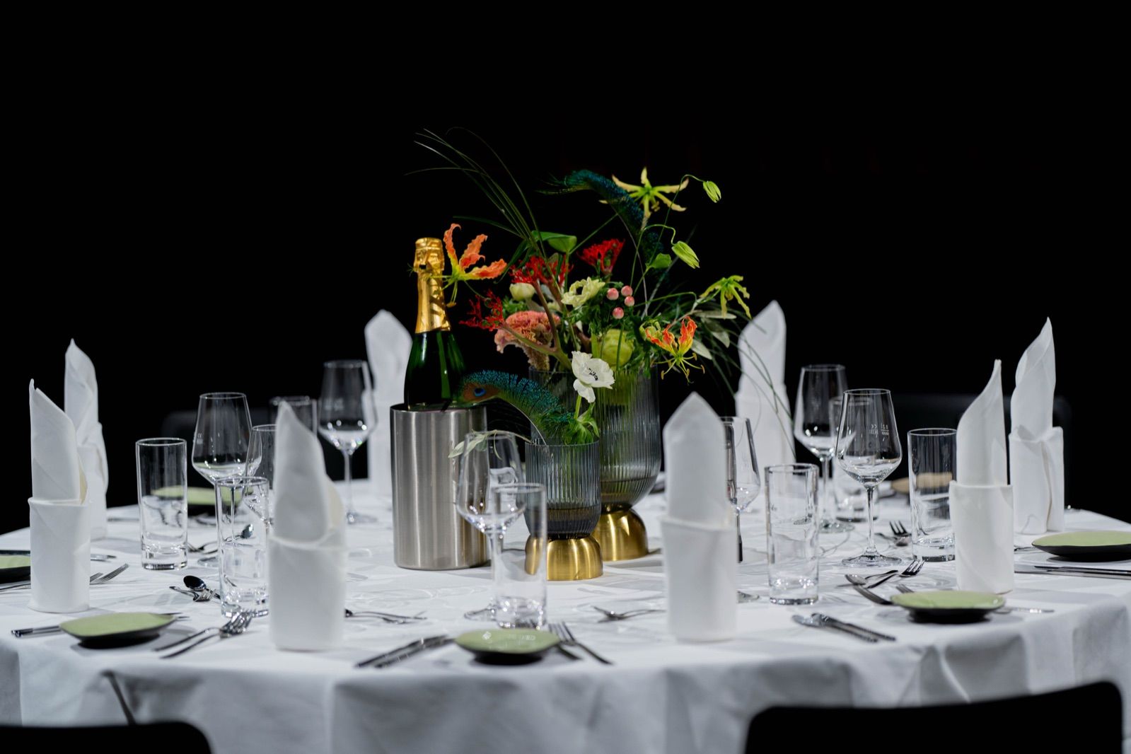 Festlich eingedeckte runde Tafel mit Blumengesteck, Sekt im Kühler und stehenden Servietten