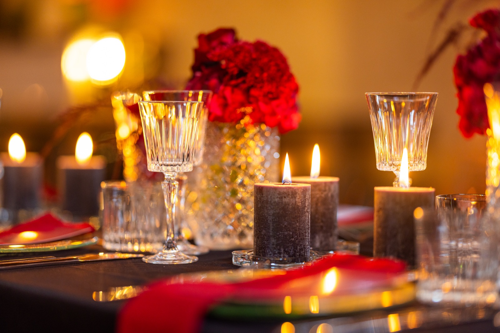 Kristallgläser, brennende Kerzen und rote Blüten auf einer festlich gedeckten Tafel