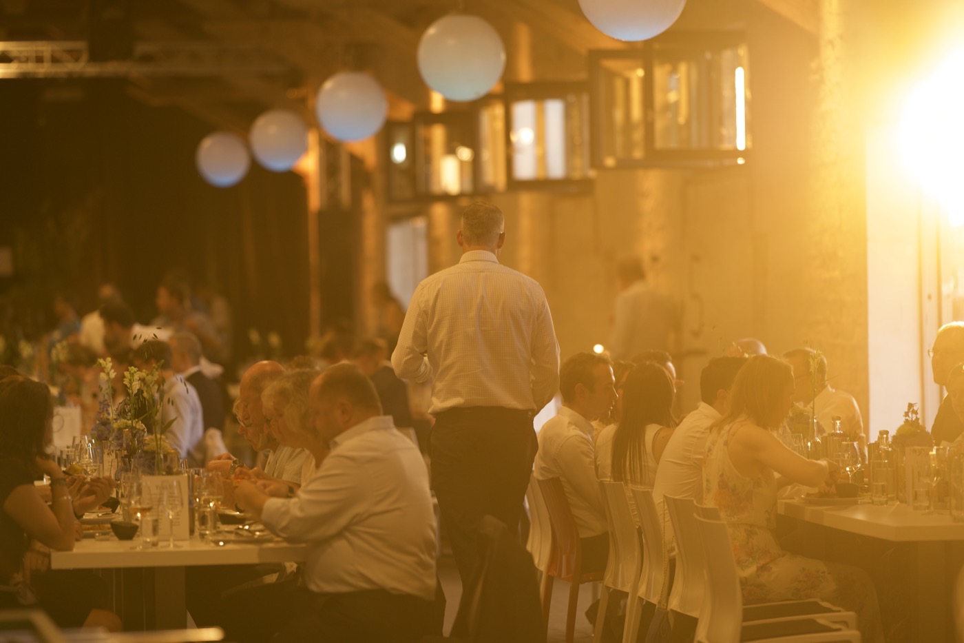 Volle Festtafeln im goldenen Abendlicht der Halle 6, Service unterwegs zwischen den Gästen