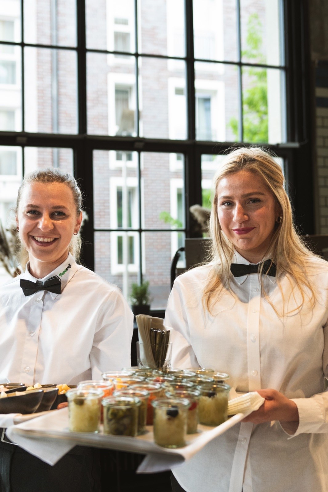 Zwei Foodcraft-Servicekräfte mit Tabletts am Fenster
