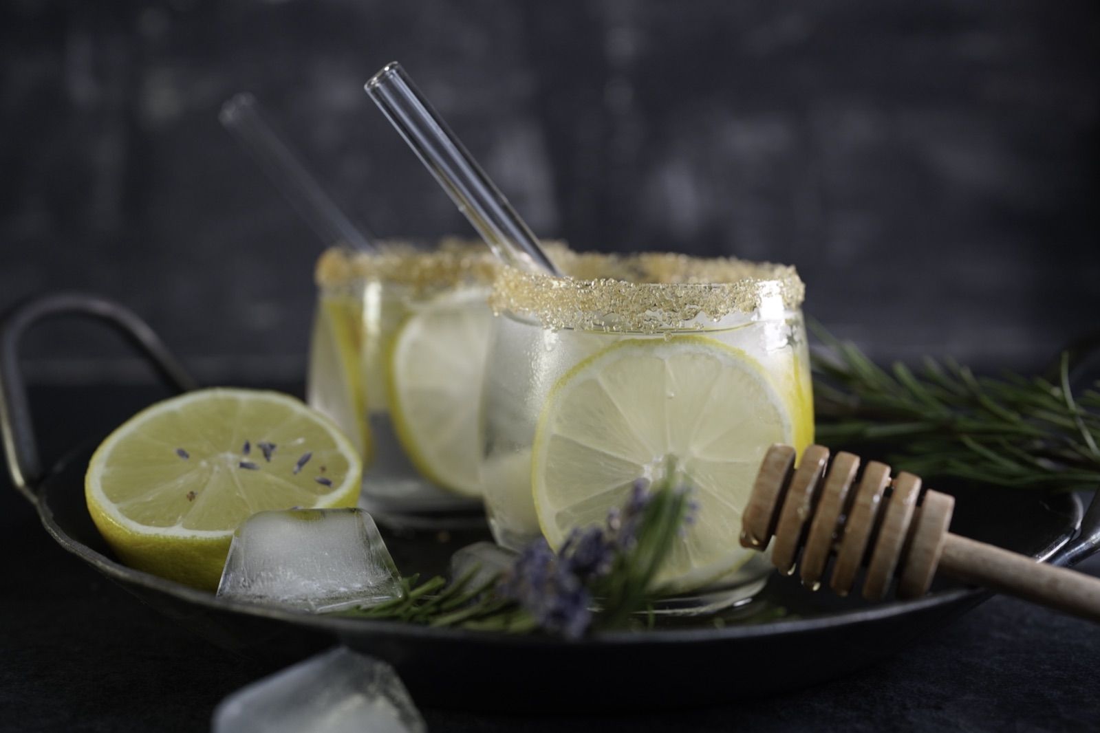Zitronenlimonade mit Zuckerrand, Lavendel und Glasstrohhalmen auf einem Tablett