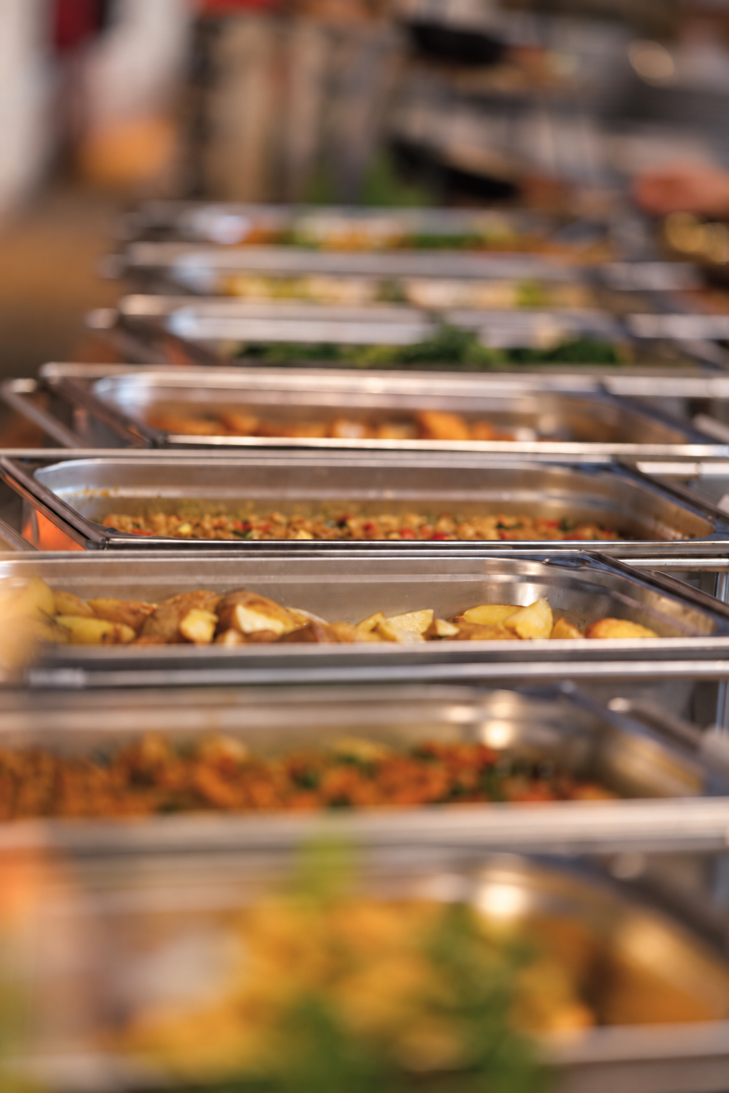 Eine Reihe geöffneter Warmhaltebehälter mit Speisen am Buffet