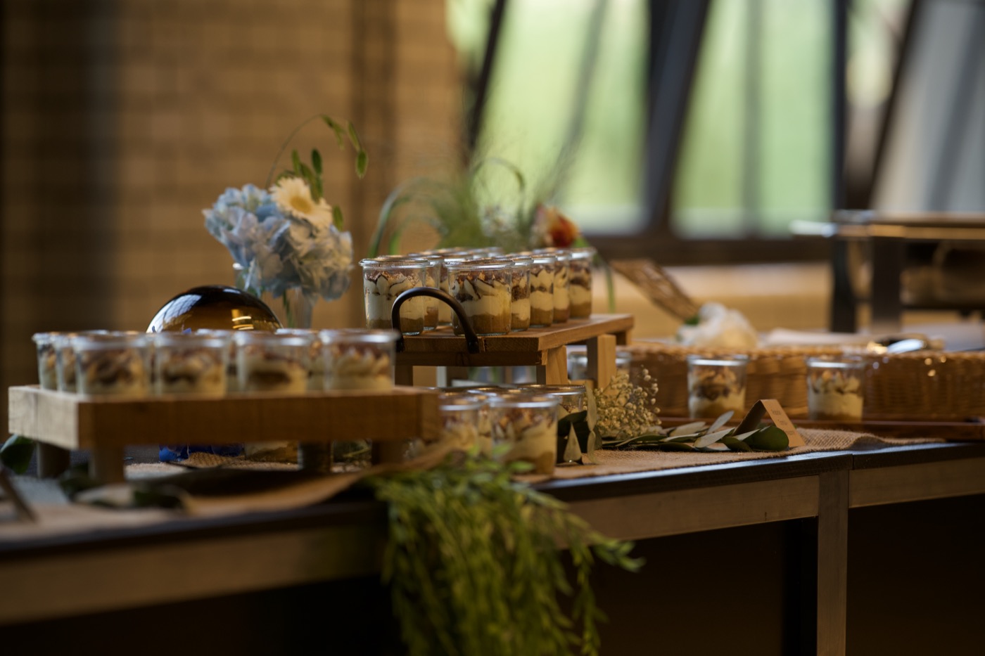 Buffet mit Dessertgläsern und Holzstegen vor einer Klinkerwand und großen Fenstern