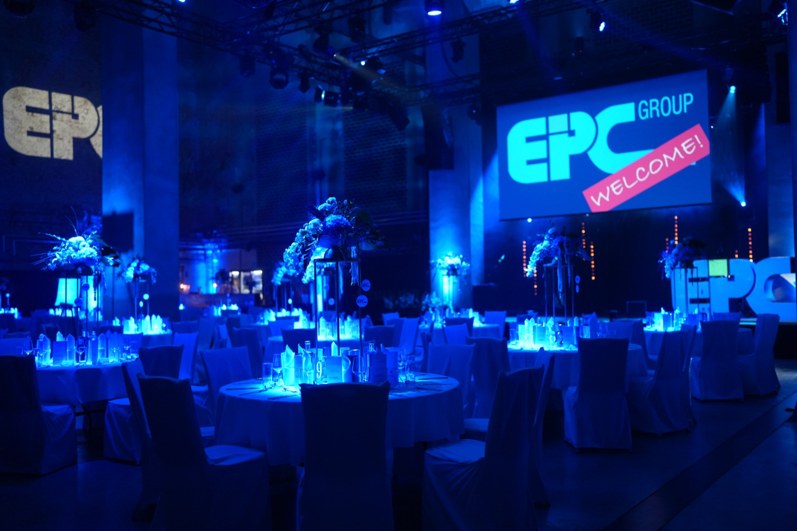 Runde eingedeckte Tafeln und eine Bühne mit EPC-Group-Willkommensanzeige im blauen Licht