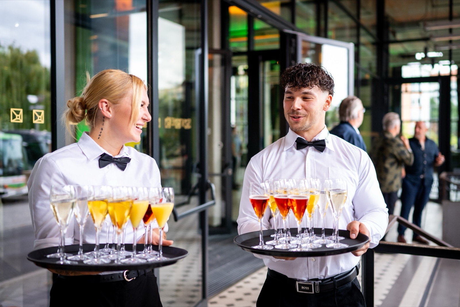 Zwei Foodcraft-Servicekräfte mit Fliege tragen Tabletts voller Aperitifs