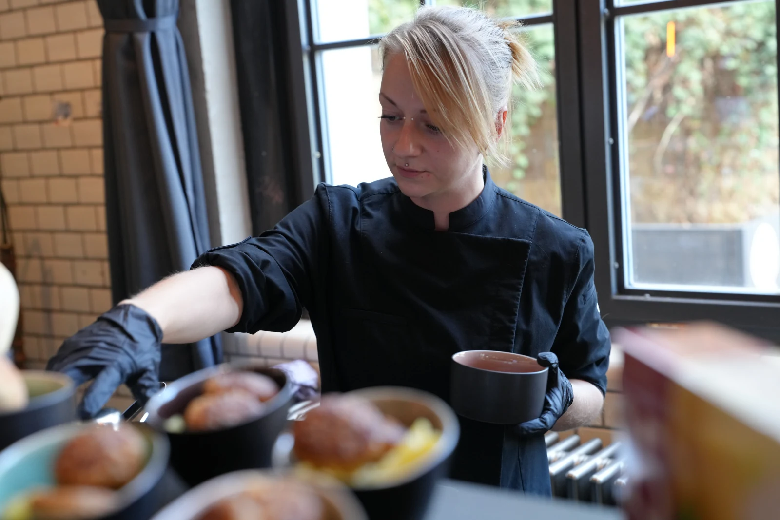Foodcraft-Mitarbeiterin in schwarzer Küchenjacke mit einer Schale an der Speisenausgabe