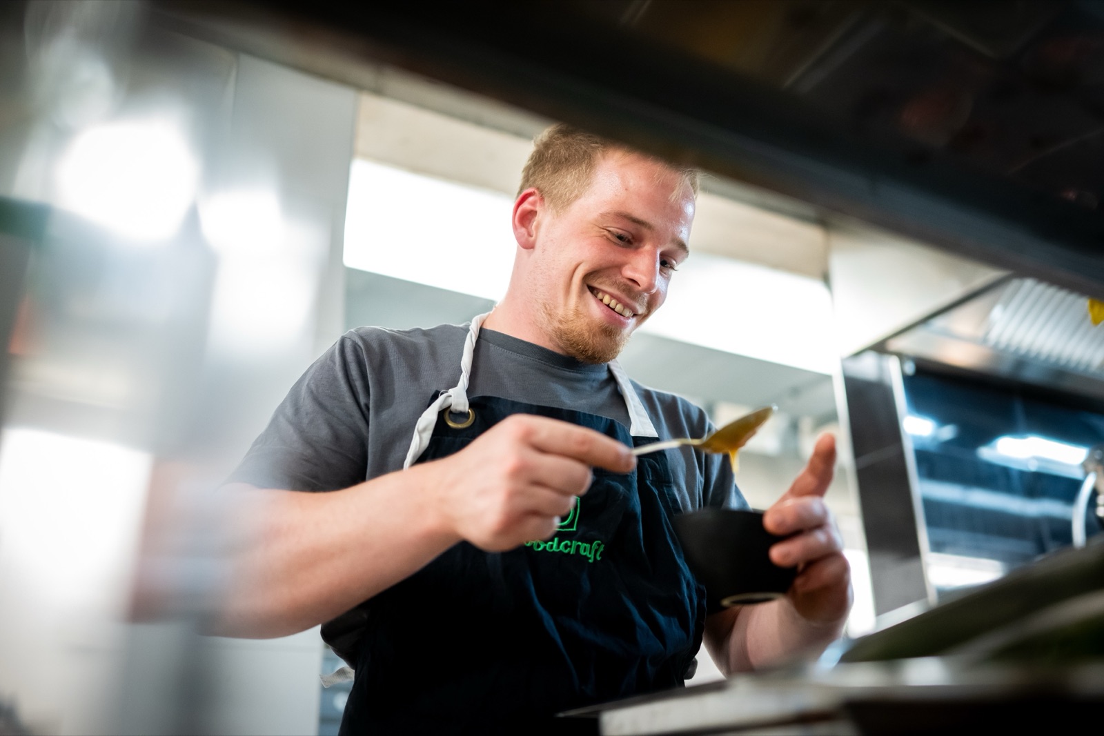 Lächelnder Foodcraft-Koch richtet mit einem Löffel ein Gericht in einer schwarzen Schale an