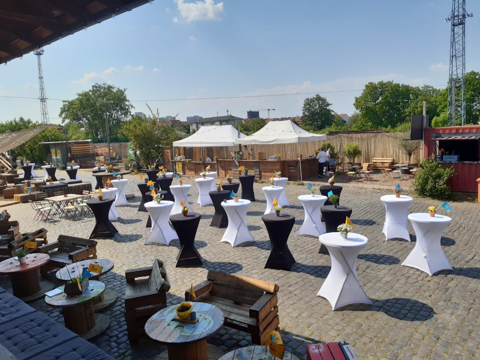 Sommerfest im Freien: eingedeckte Stehtische mit Blumen, Pagodenzelte und Bar