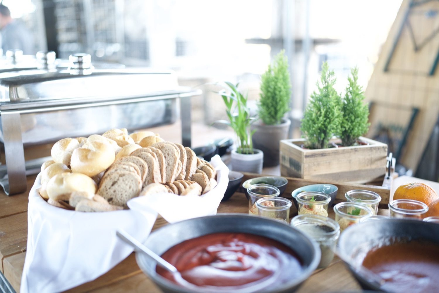Helles Tagesbuffet am Fenster: Brotkörbe, Dips in Gläsern und warme Speisen im Chafing