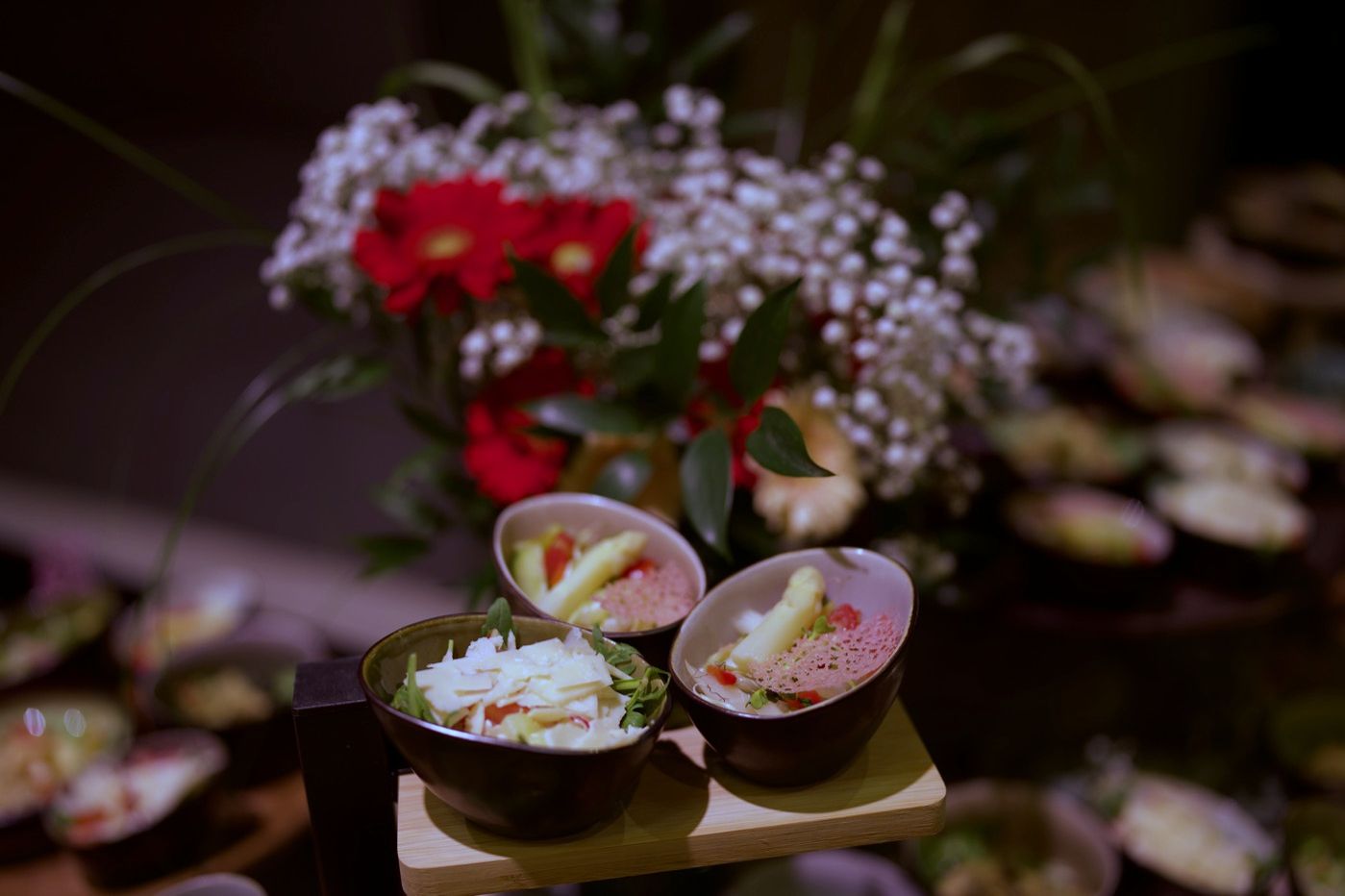 Buffet mit Salatschalen auf Holzbrettern, dahinter rote Blumen und Schleierkraut